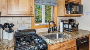 Una cocina con armarios de madera, estufa a gas, microondas y ventana con vista a árboles.