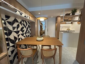 Ein moderner Essbereich mit einem Holztisch, Korbstühlen, einer Wand mit geometrischem Muster und einer Küche im Hintergrund.