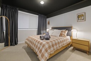 Un dormitorio con cama, mesita de noche, lámpara, ventana con cortinas y un cuadro en la pared.