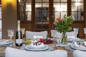 Una mesa de comedor elegantemente dispuesta con una botella de champán, un centro de mesa floral y una variedad de frutas y quesos.