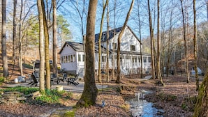 Een chalet met een veranda, omgeven door bomen en een beekje.