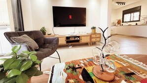 Moderni olohuone, jossa on litteänäyttöinen televisio, mukava sohva, ruokailutila pöytineen ja taustalla keittiö.