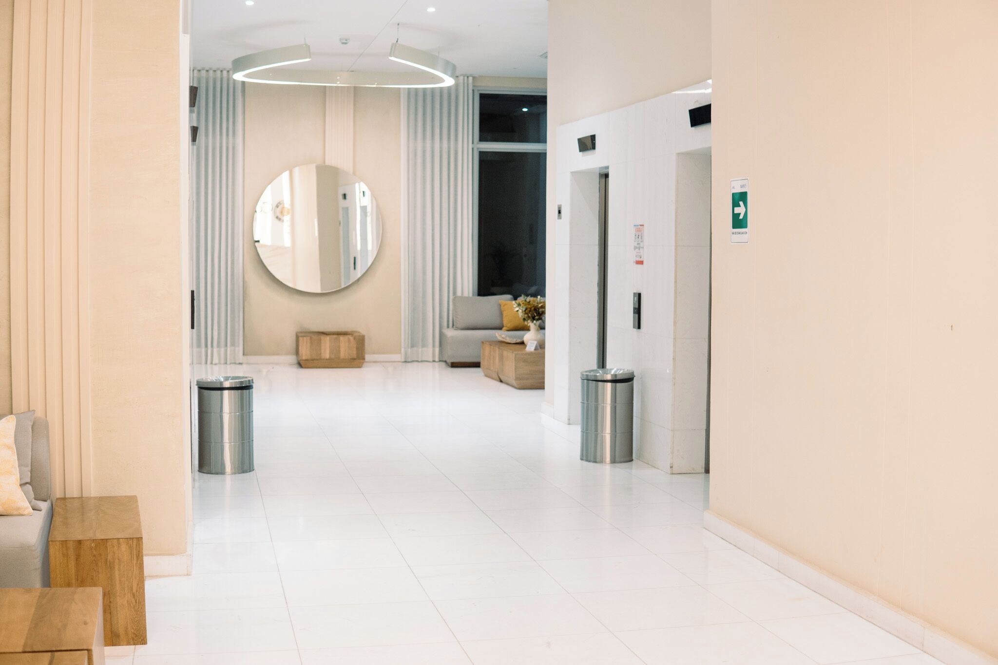 A modern hotel lobby with a clean, minimalist design, featuring a large mirror, a sofa, and a trash bin.