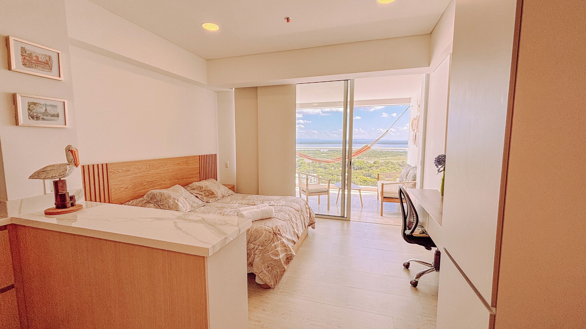 A bedroom with a bed, a desk, and a chair. There is a view of the outdoors through a glass door.
