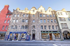 A historic stone building with multiple stories, featuring a prominent entrance and several ground-level shops including 'Prestige Scotland' and 'Thistle do Nicely'. - Charming City Apartment on Royal Mile (Edinburgh)