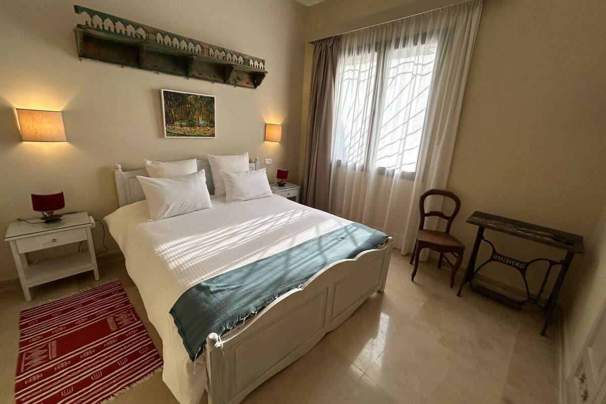 A neatly arranged bedroom with a large bed, bedside lamps, a desk, and a chair.