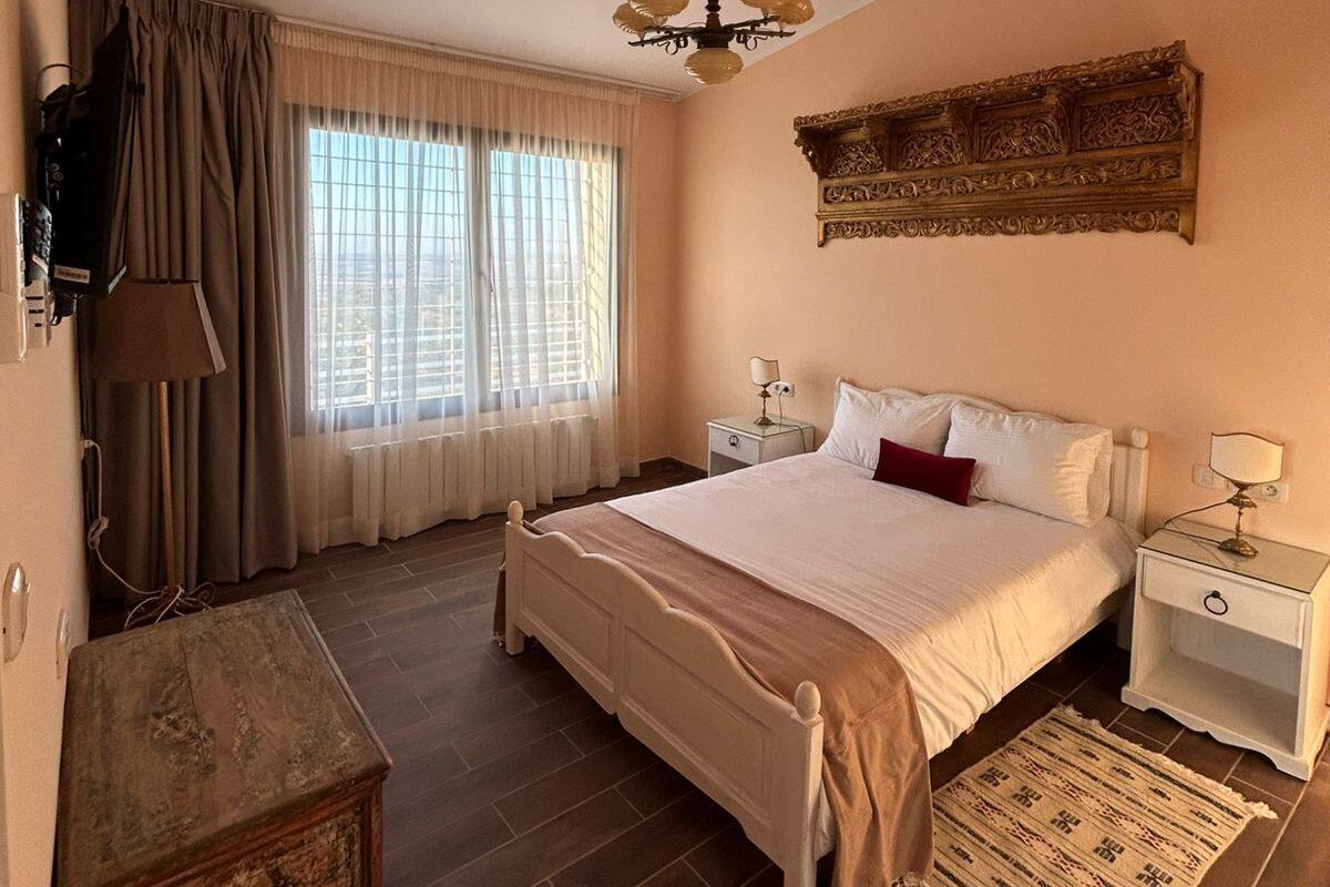 A bedroom with a large bed, a nightstand, a dresser, a ceiling fan, and a window with curtains.