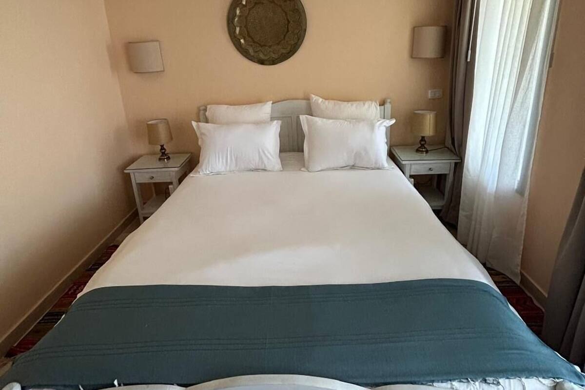 A hotel room with a large bed, two bedside tables, a wall-mounted decorative plate, and a window with curtains.