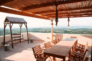 A wooden deck with a table and chairs, a wooden bench, and a hanging light fixture. - Dar Nesri (Zaghouan)
