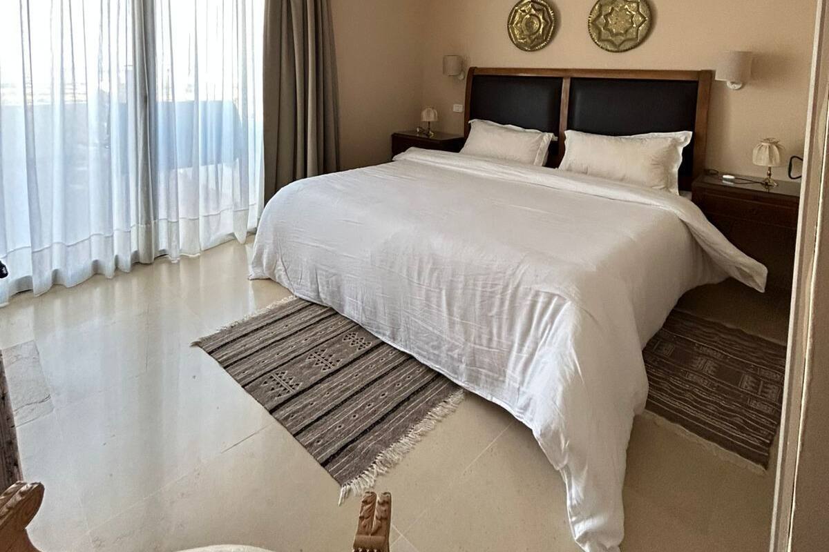 A hotel room with a large bed, a chandelier, a view of the city, and two decorative plates on the wall.