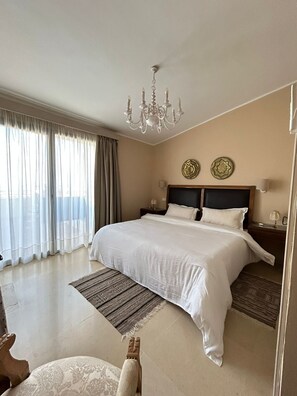 A hotel room with a large bed, a chandelier, a view of the city, and two decorative plates on the wall. - Dar Nesri (Zaghouan)