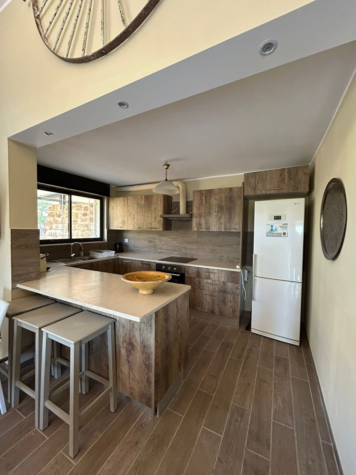 Een moderne keuken met een centraal eiland, barstoelen, een inbouwoven en een koelkast.