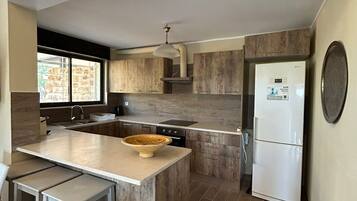 Een moderne keuken met een centraal eiland, barstoelen, een inbouwoven en een koelkast.