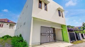 Une maison moderne à deux étages, avec une façade blanche, une porte verte et un portail noir.