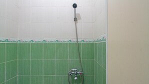 Une douche équipée d’un flexible et d’un pommeau de douche fixé au mur, dans une pièce dont les murs sont recouverts de carreaux verts.