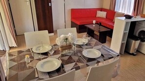 Un espace de vie compact comprenant un coin repas, un canapé rouge, un lave-linge et un coin cuisine.