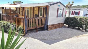 Une maison mobile dotée d’une terrasse en bois, d’un porche couvert et d’une allée en gravier.