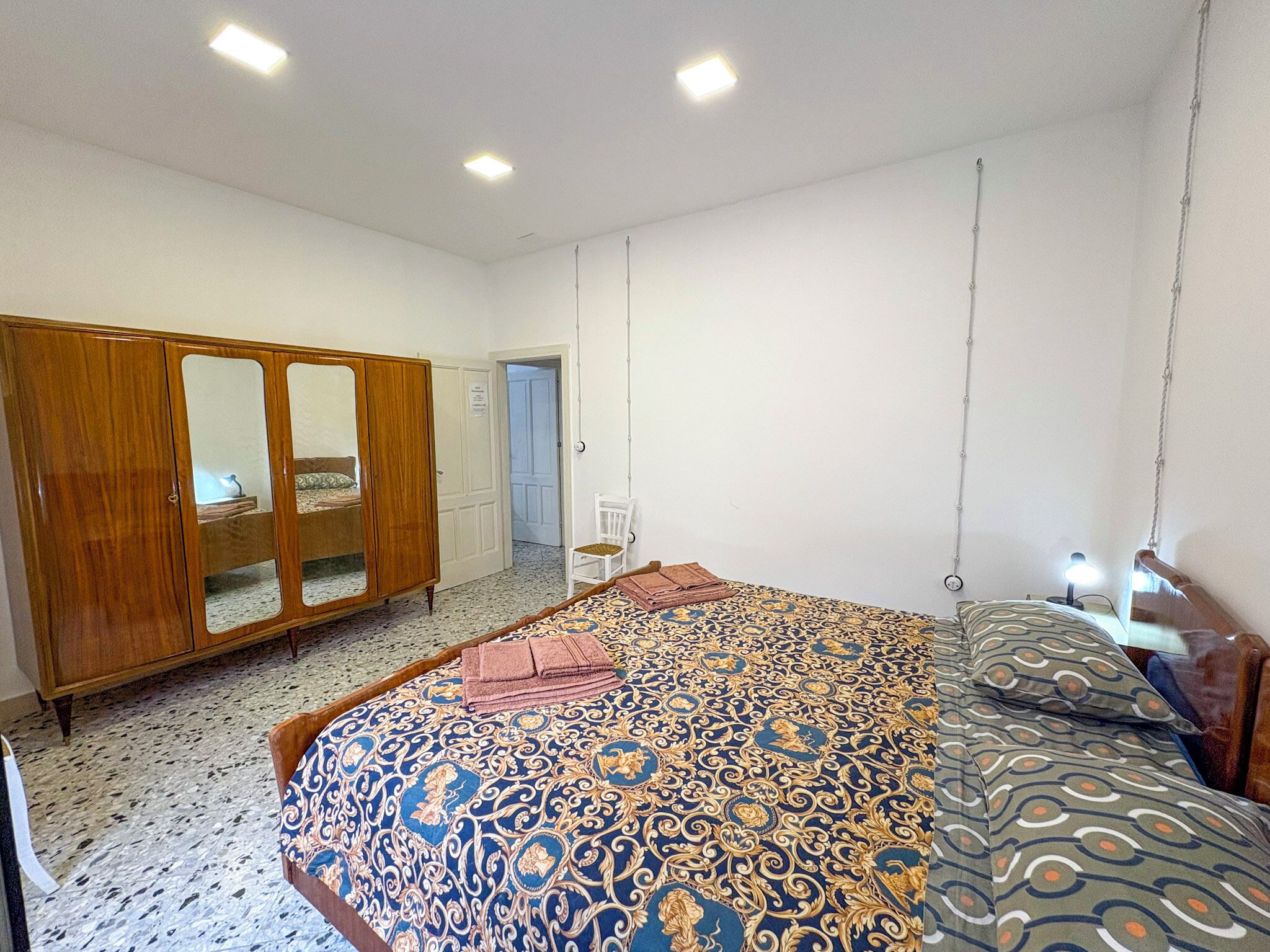 Une chambre à coucher avec un grand lit, une armoire, une chaise et un luminaire suspendu.