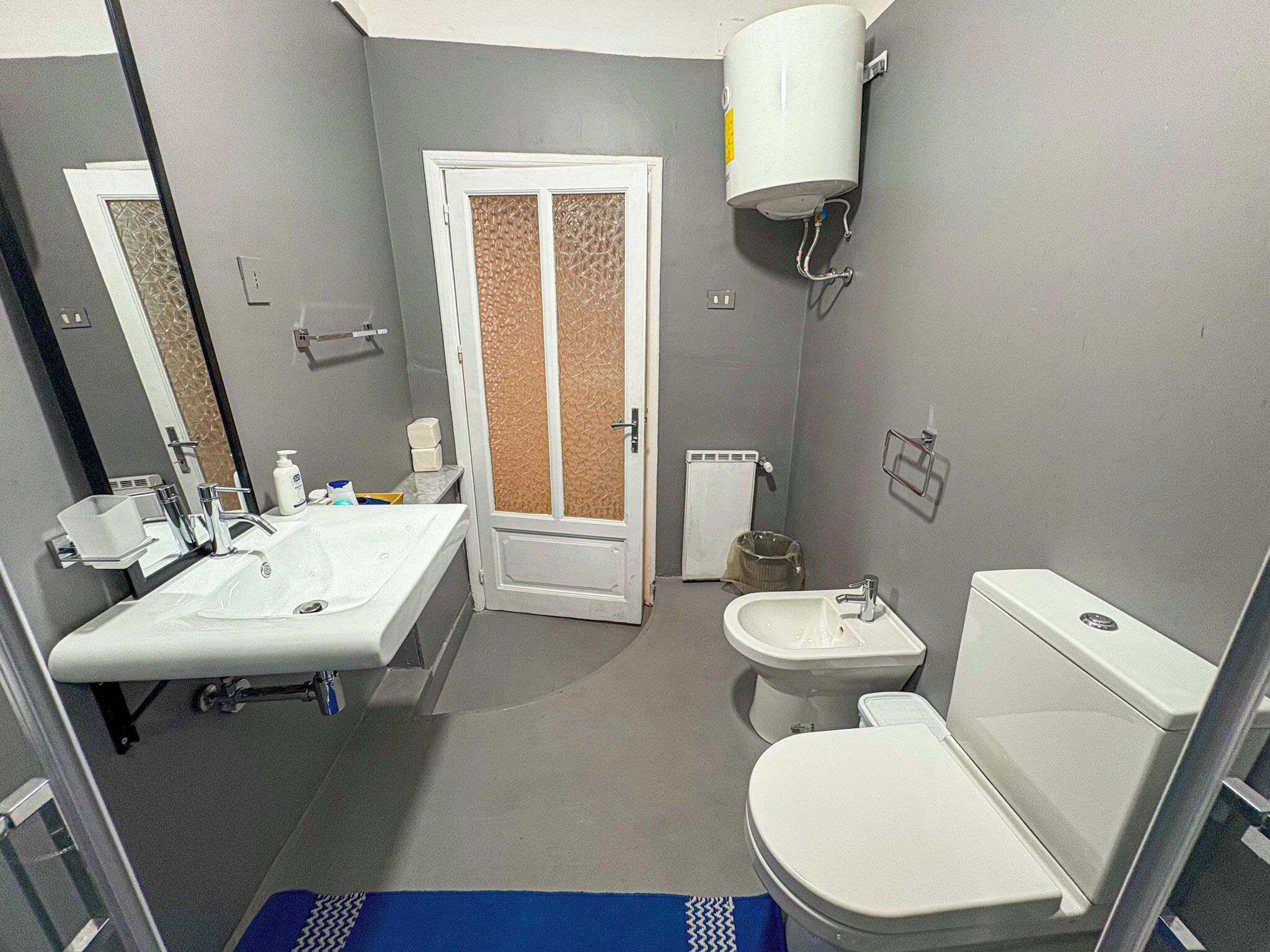 A bathroom with a white sink, a toilet, and a bidet. There is a mirror above the sink and a towel rack on the wall.