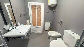 A bathroom with a white sink, a toilet, and a bidet. There is a mirror above the sink and a towel rack on the wall.