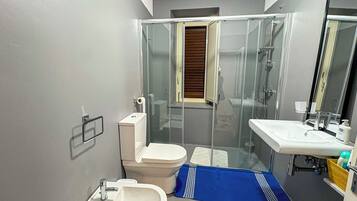 Une salle de bain comprenant des toilettes, un bidet, un lavabo et une douche à parois de verre.