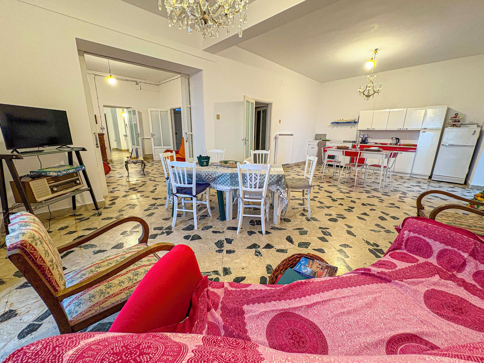 A living room with a TV, a dining area with a table and chairs, a kitchen with a fridge and stove, and a patterned floor.