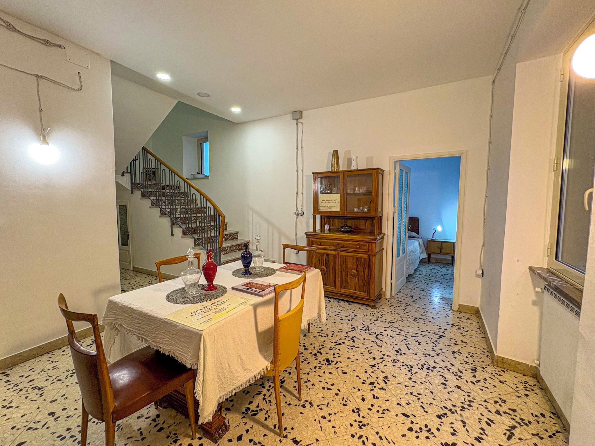 Un comedor con una mesa dispuesta para dos, un armario de madera y una escalera que sube a otra habitación.