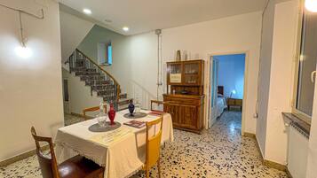 Un comedor con una mesa dispuesta para dos, un armario de madera y una escalera que sube a otra habitación.