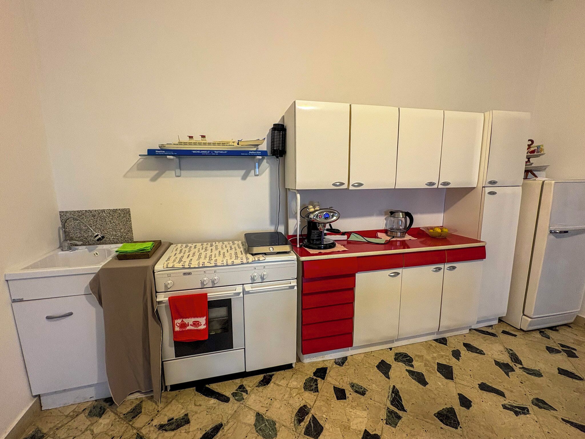 Una cocina compacta con gabinetes blancos, encimera roja, un lavamanos y un refrigerador pequeño.