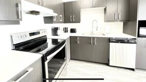 Una cocina moderna con electrodomésticos de acero inoxidable, muebles grises y encimera blanca.