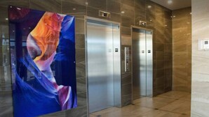 Un área de ascensor moderna con suelo de mármol y un gran cuadro abstracto en la pared.
