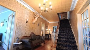 Un vaste hall d’entrée avec un escalier, un canapé, un lustre et une tête de cerf fixée au mur.