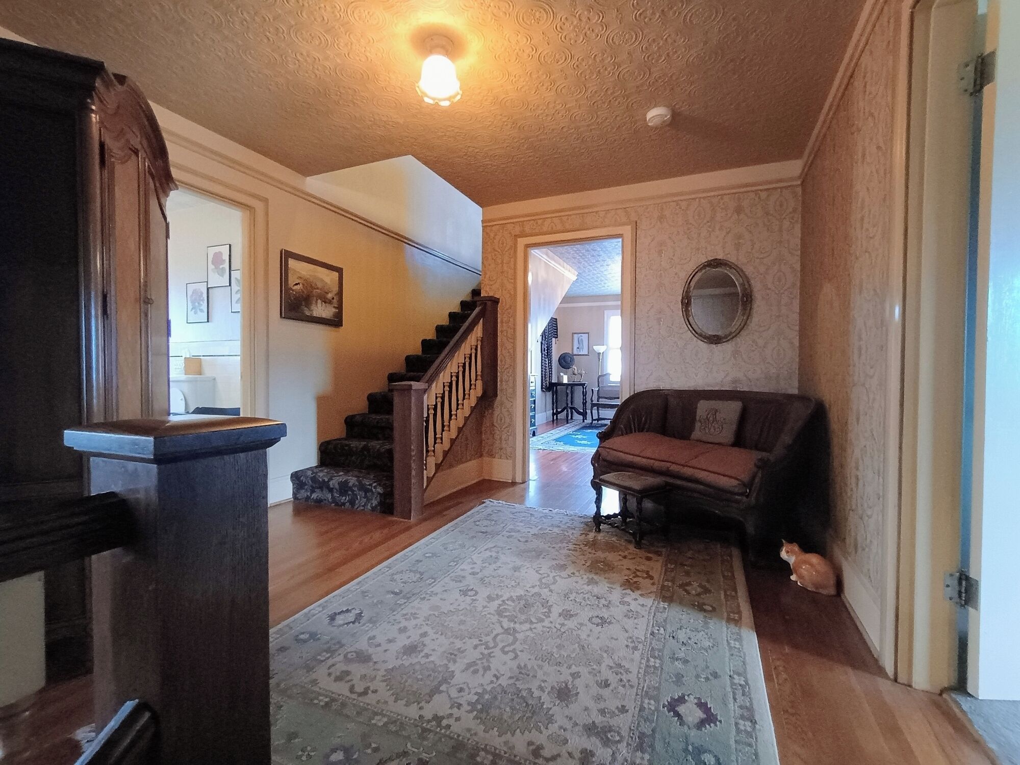 A spacious living area with a wooden staircase, a patterned rug, a sofa, and a mirror on the wall.
