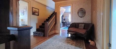 A spacious living area with a wooden staircase, a patterned rug, a sofa, and a mirror on the wall.