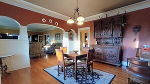 Un amplio comedor con una mesa y sillas de madera, un tapete estampado y una cocina con armarios ornamentales.