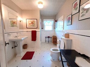 A bathroom with a toilet, sink, and bidet. There are framed pictures on the walls and a red towel hanging on the sink.