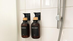Een badkamer met twee shampoos en douchegels bevestigd aan de muur, een chromen douchekop en een handdouche.