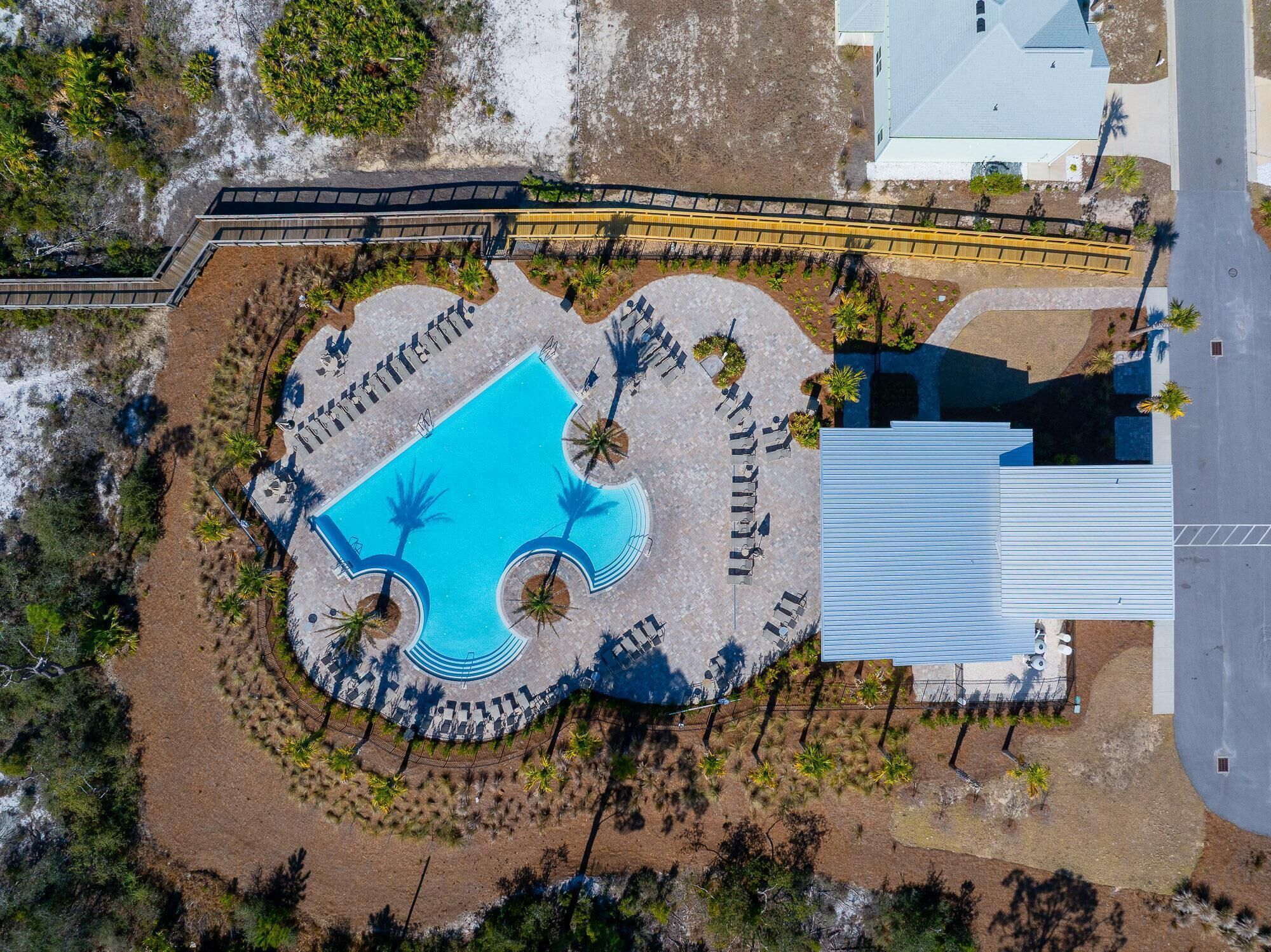 An aerial view of a resort with a central pool, palm trees, and a large building.