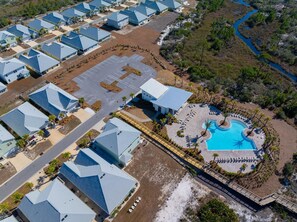 Vista aerea di un resort con diversi edifici dai tetti blu, un'area piscina centrale con lettini e un paesaggio naturale circostante.