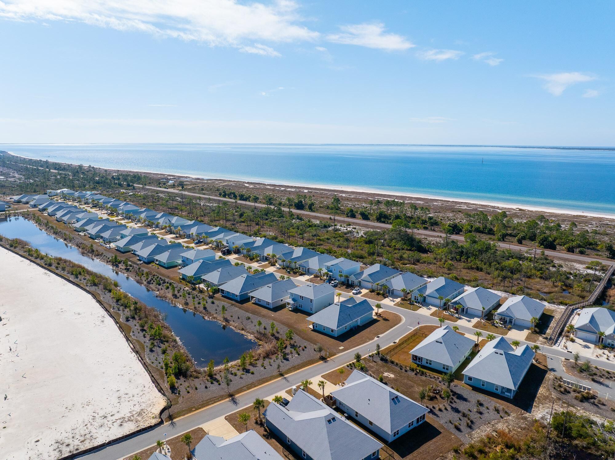 Eine Luftaufnahme eines Küstenresorts mit mehreren Gebäuden mit blauen Dächern, die in Reihen angeordnet sind, einem Strand und freier Sicht auf den Ozean.