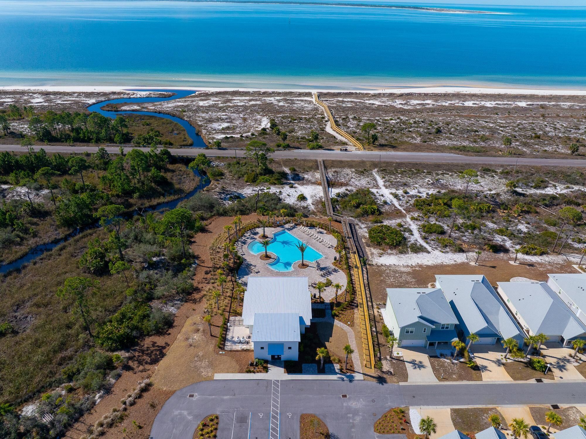 An aerial view of a coastal resort with a swimming pool, a parking area, and beachfront properties.