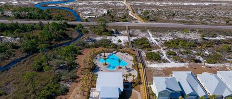An aerial view of a coastal resort with a swimming pool, a parking area, and beachfront properties.