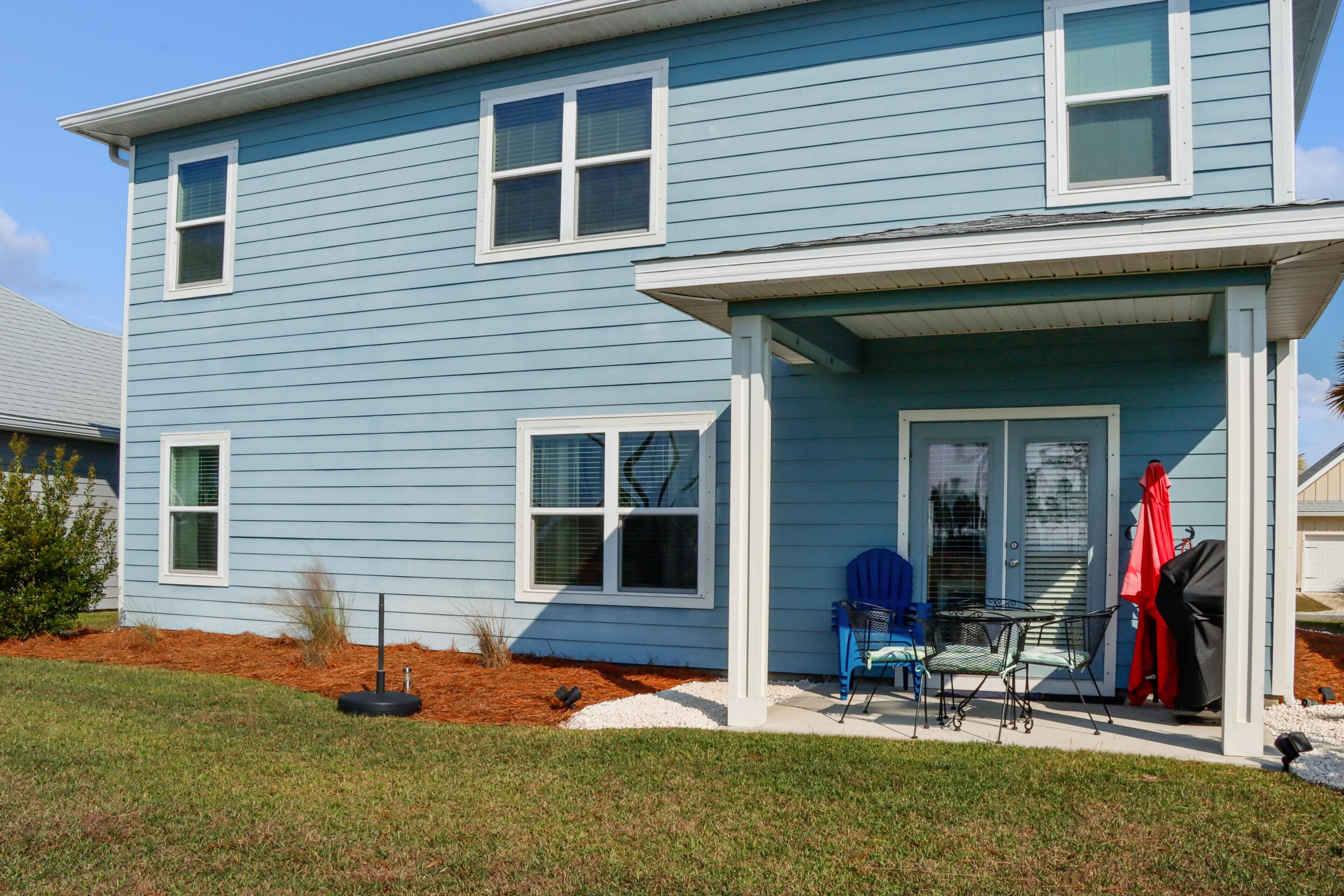 A two-story house with a covered porch, a small patio with a table and chairs, and a red barbecue cover.