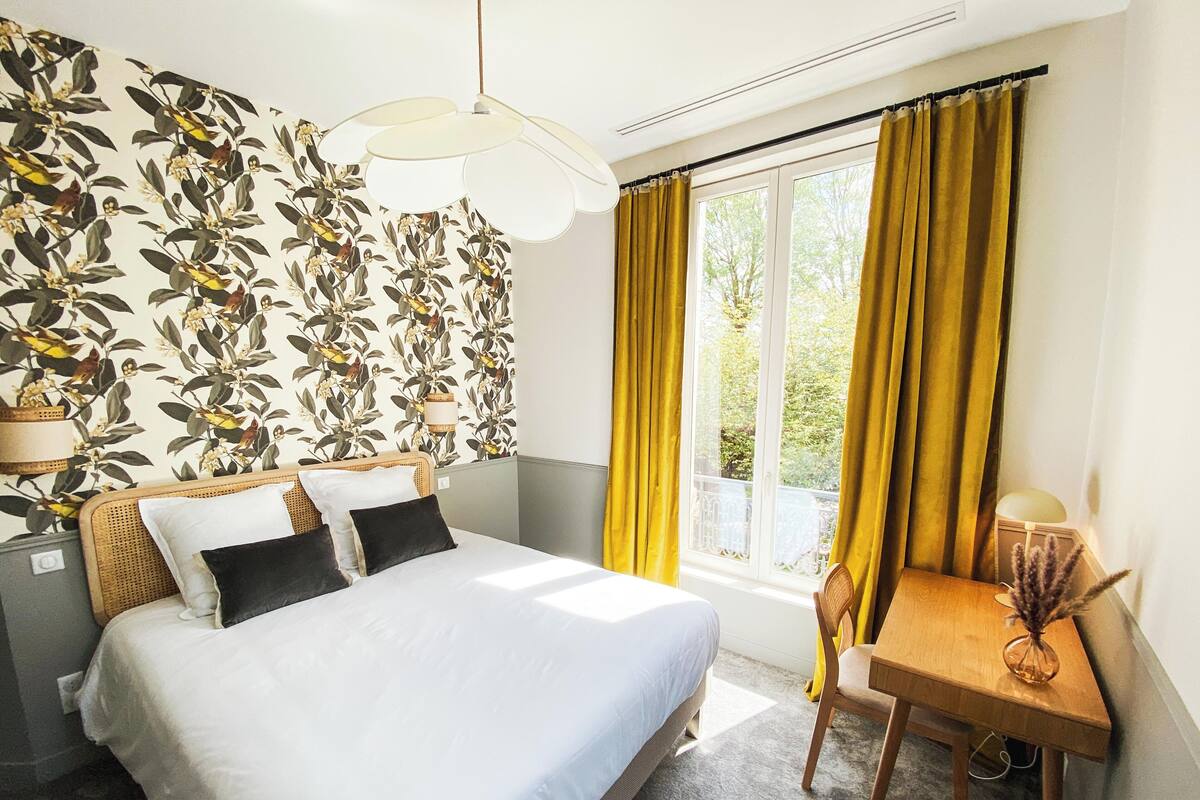 A bedroom with a bed, a desk, a chair, a lamp, and a window with curtains.