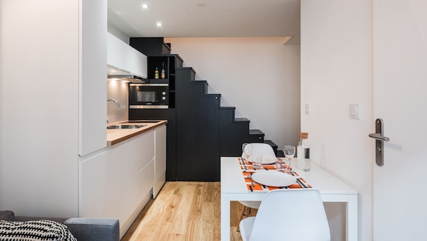 A compact kitchen with modern appliances, a dining area with a white table and chairs, and a staircase leading to an upper level. - SmartStay Perrache - Presqu'île (Lyon)