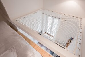 Ein Zimmer mit einem Bett, einem weißen Insektenschutznetz am Fenster und einem Holzboden.
