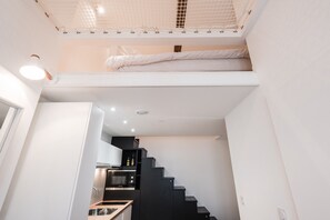 Ein kompakter, moderner Raum mit Etagenbett, Küchenzeile und einer Treppe zu einer erhöhten Ebene.