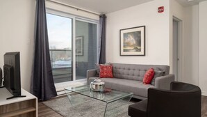 Una sala de estar moderna con una mesa de centro de vidrio, un sofá gris con cojines rojos, un sillón negro y un televisor de pantalla plana sobre un mueble de madera.