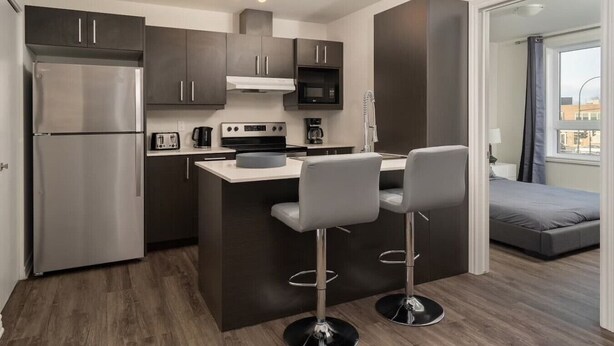 Cocina compacta equipada con refrigerador, microondas, estufa y taburetes de bar.