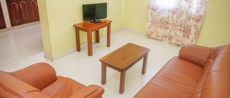 A living room with a sofa, two armchairs, a coffee table, and a TV on a stand.